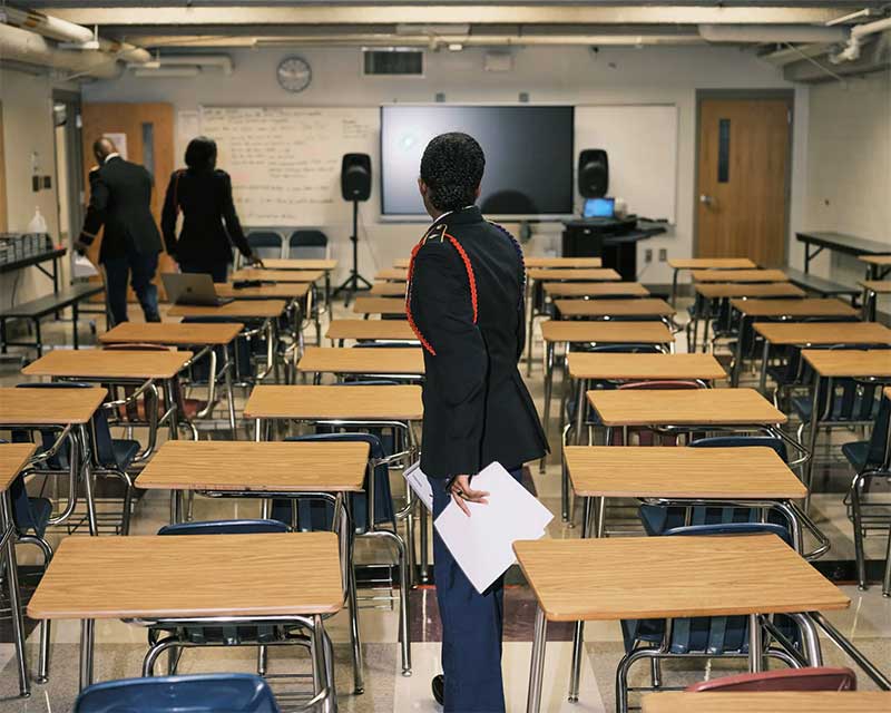 A uniformed J.R.O.T.C. student stands in a sea of desks in a mostly empty classroom.